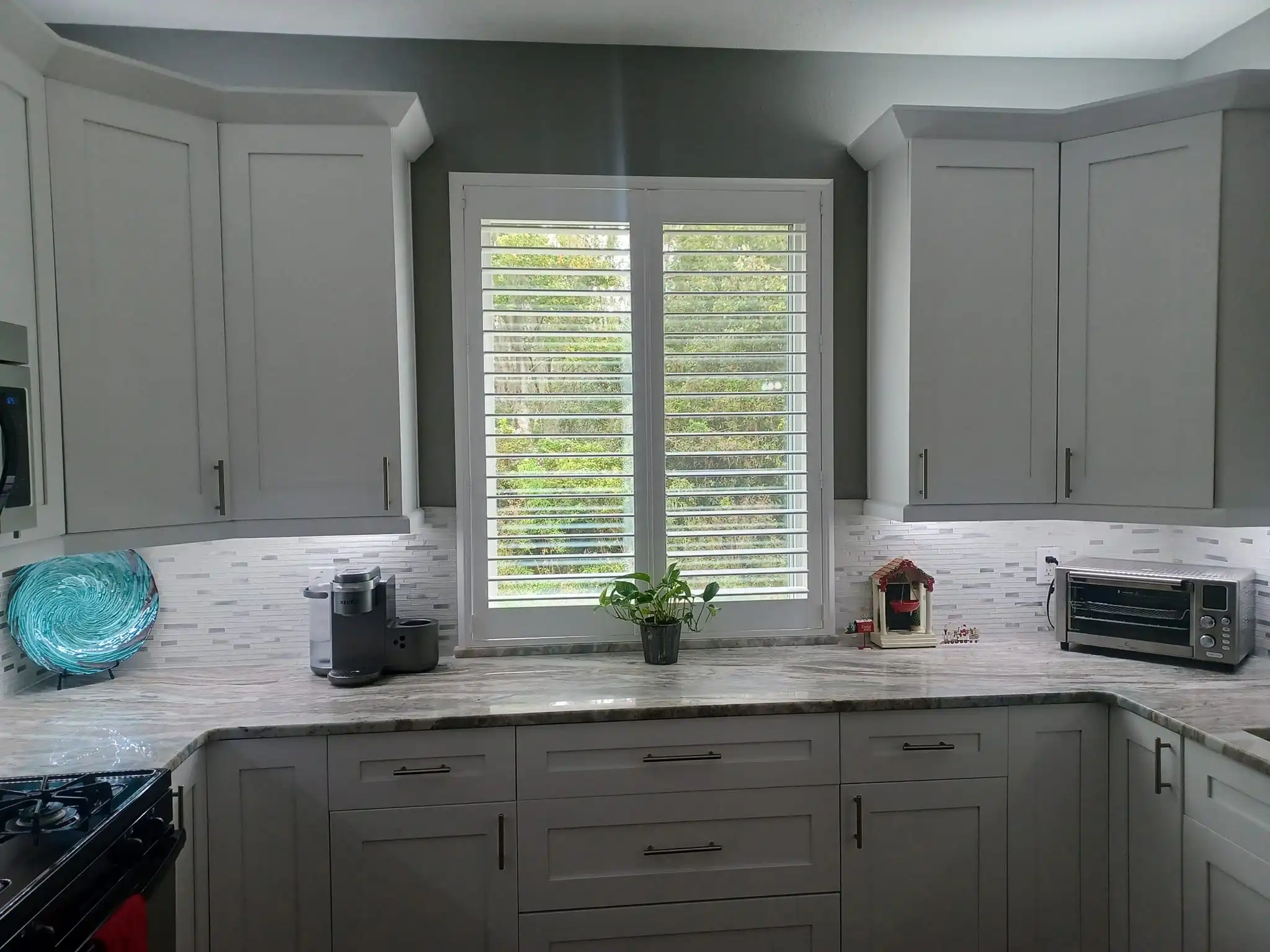 Modern kitchen in Lakeland featuring light gray cabinets, a marble countertop, and a window with white plantation shutters