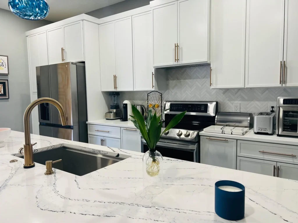 Modern Lakeland kitchen with white cabinets, stainless steel appliances, marble countertops, a sink with gold faucet, and a vase with flowers on the island—perfect for stylish living in FL.
