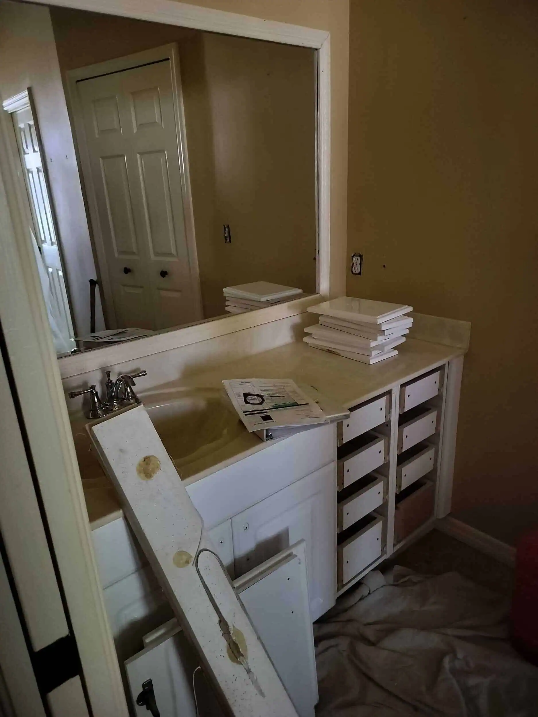 A bathroom vanity in Lakeland, FL with cabinet drawers removed, stacked drawer fronts, and tools on the counter. A sink and large mirror are visible; renovation work appears to be in progress.