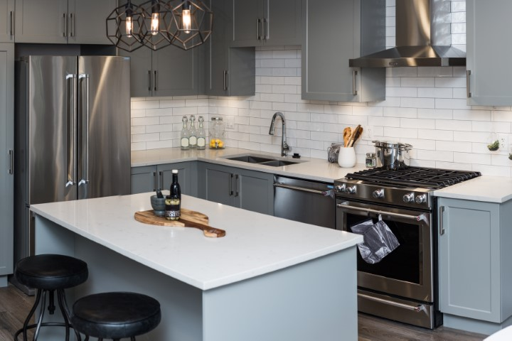 Modern Lakeland kitchen with gray cabinets, stainless steel appliances, white subway tile backsplash, and a white island with two black stools; pendant lights hang above the island in this FL home.