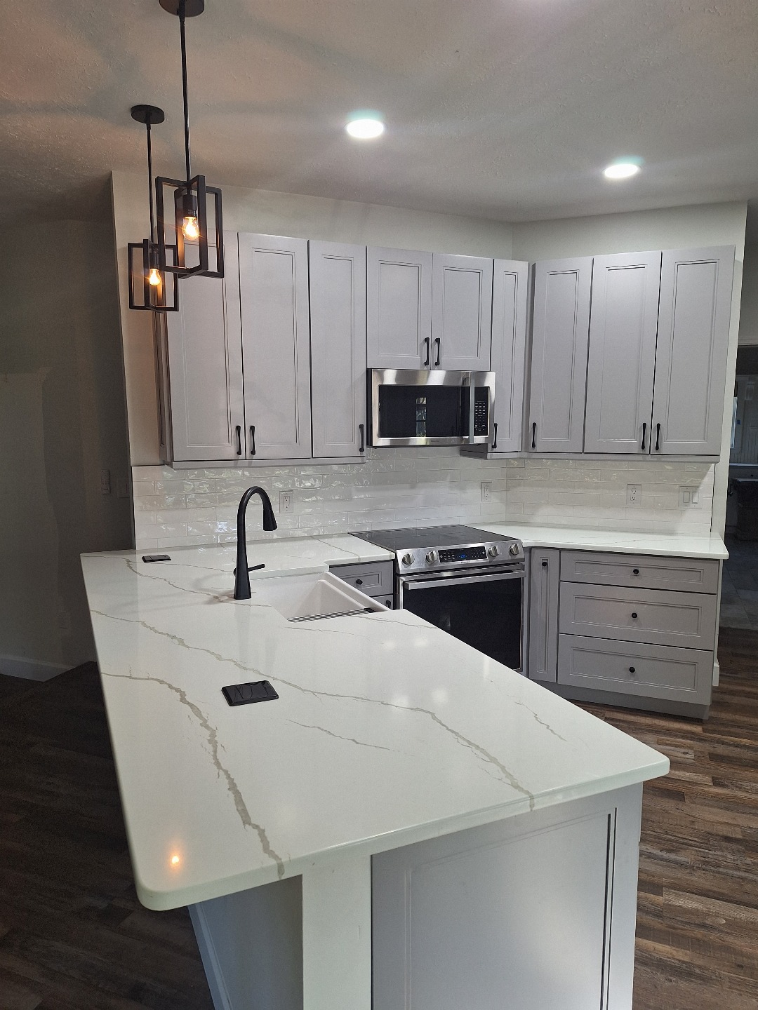 Modern Lakeland kitchen with white cabinets, white marble-patterned countertops, black fixtures, stainless steel appliances, and pendant lighting over an island—an elegant FL living space.
