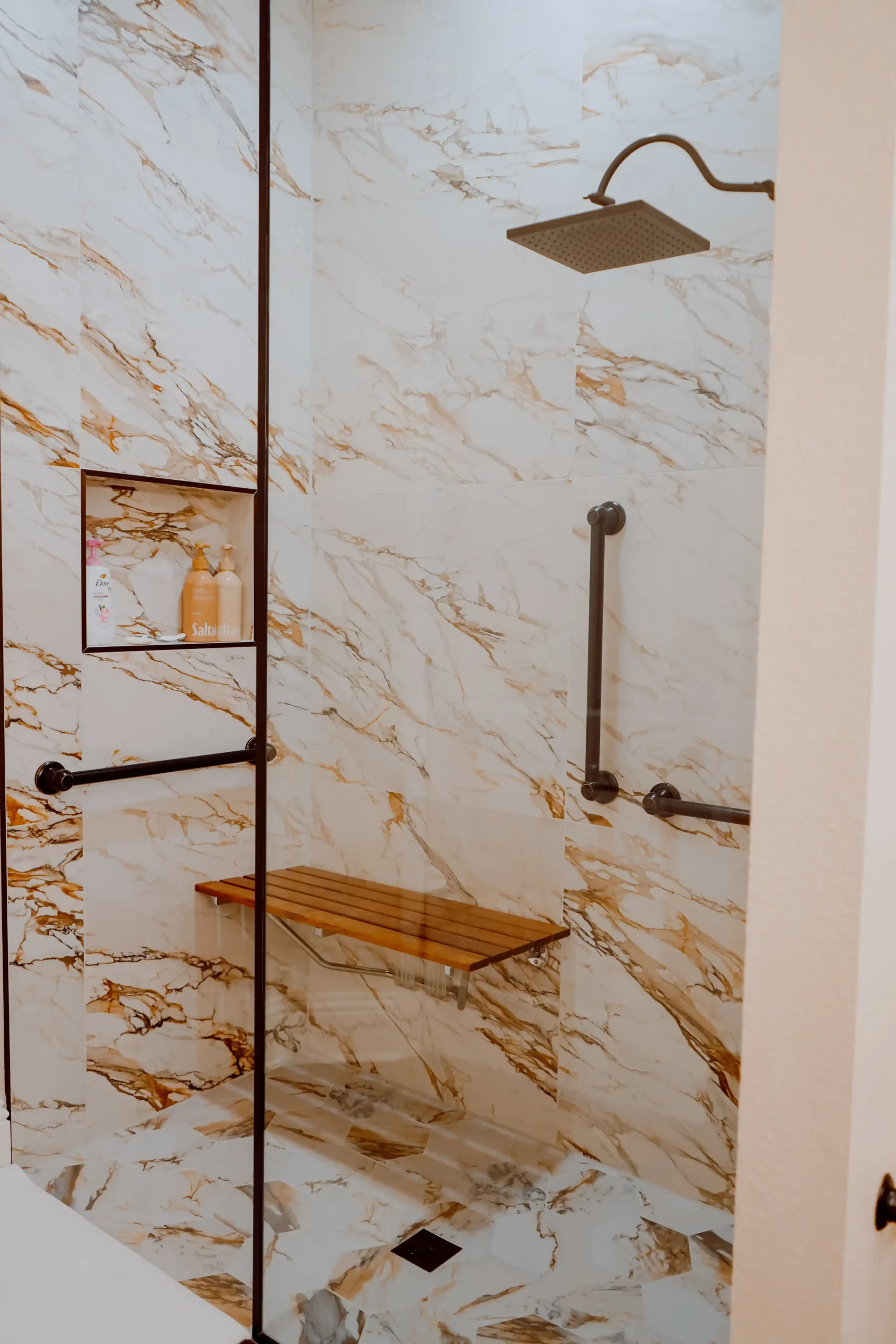 Accessible walk-in shower with marble-patterned walls, a rainfall showerhead, grab bars, and a fold-down bench in an in-law suite bathroom