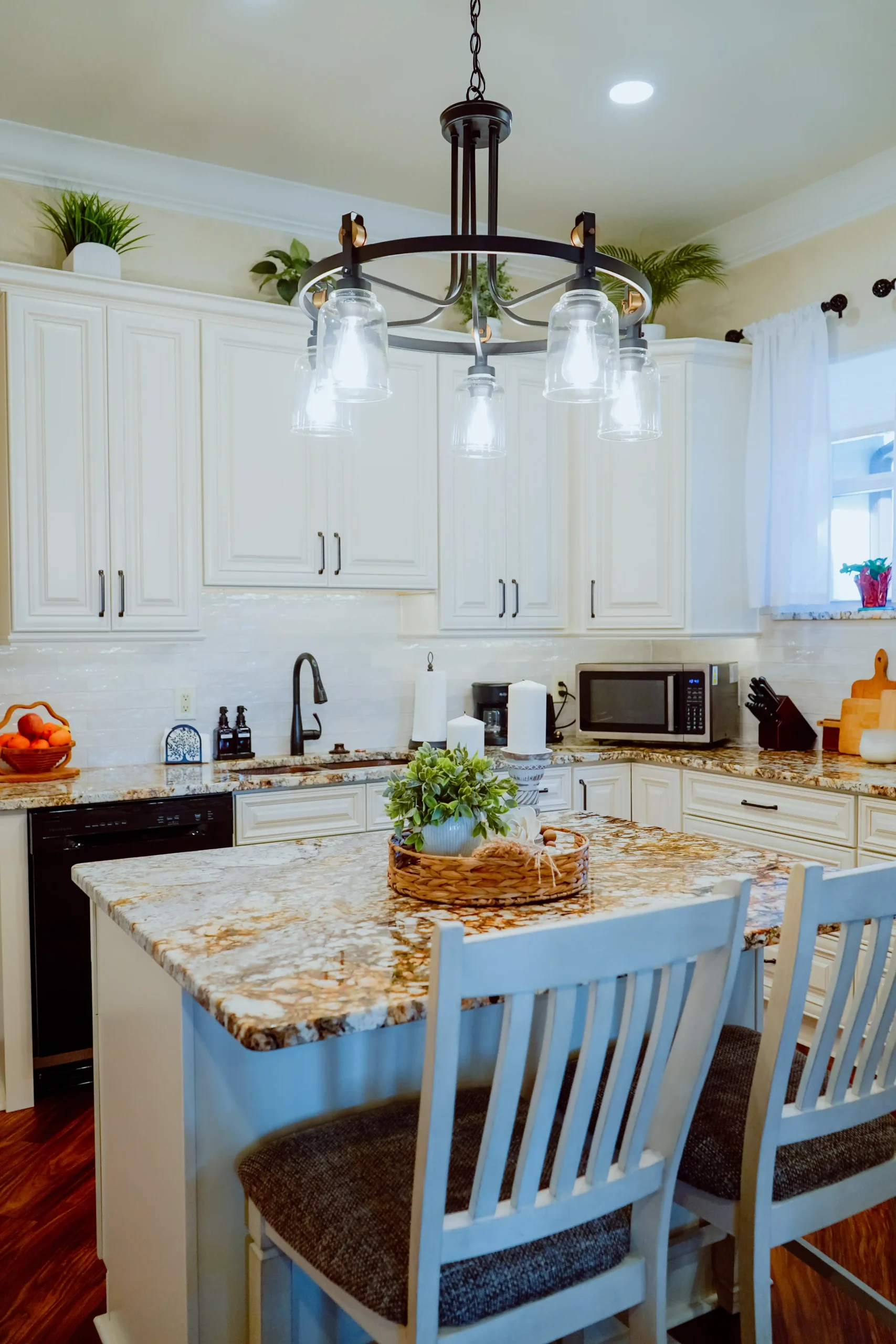 Modern mother-in-law suite kitchen with white cabinets, granite countertops, an island with two chairs, and hanging lights