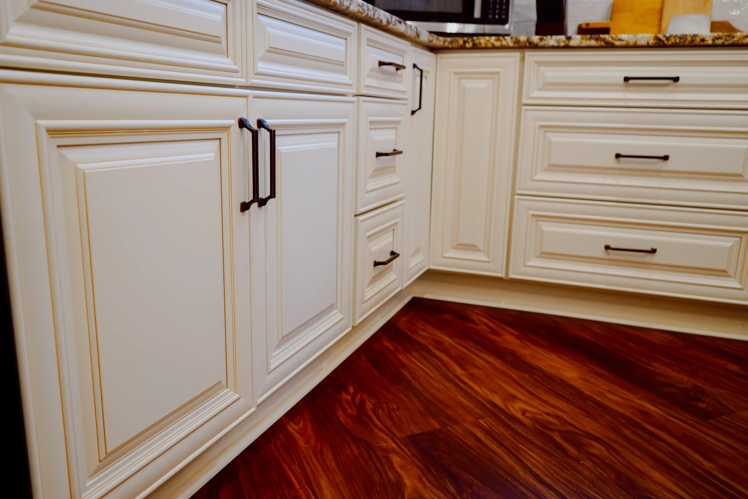 Cream-colored mother-in-law suite kitchen cabinetry with black handles, a granite countertop, and dark wood flooring